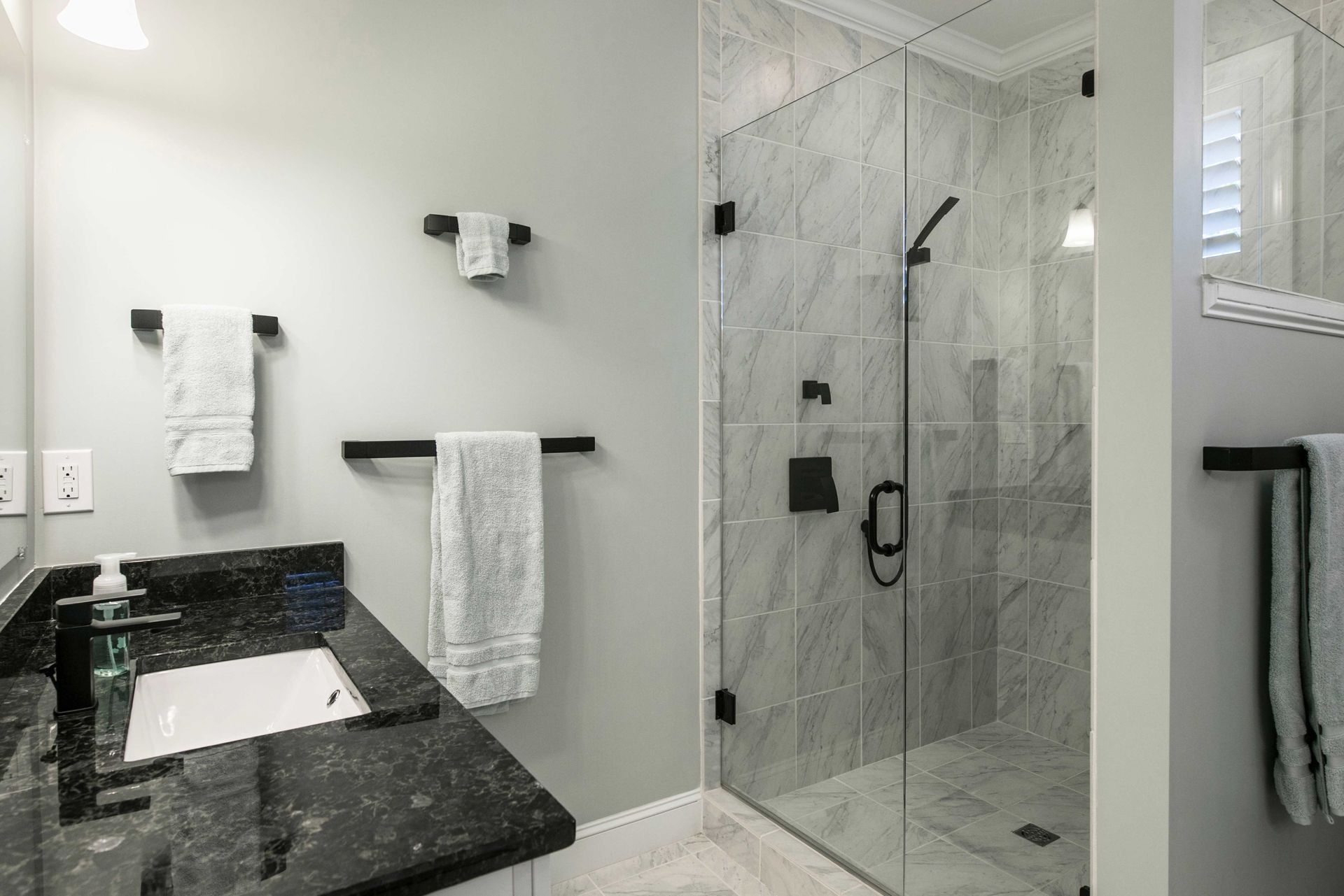 Modern bathroom with black vanity, white towels, and a glass-enclosed marble shower.