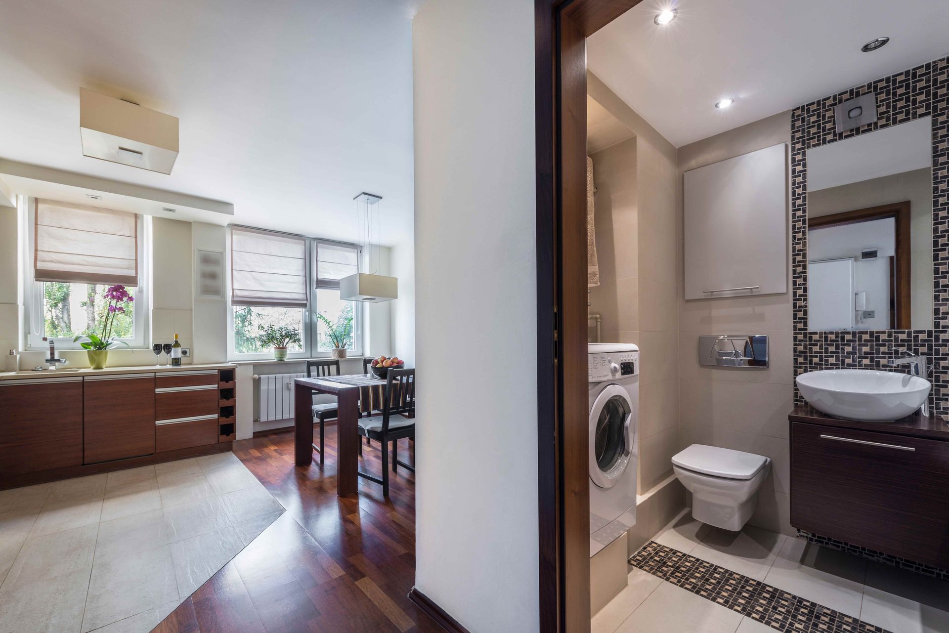 Modern apartment interior with kitchen, dining area, and compact bathroom visible through an open doorway