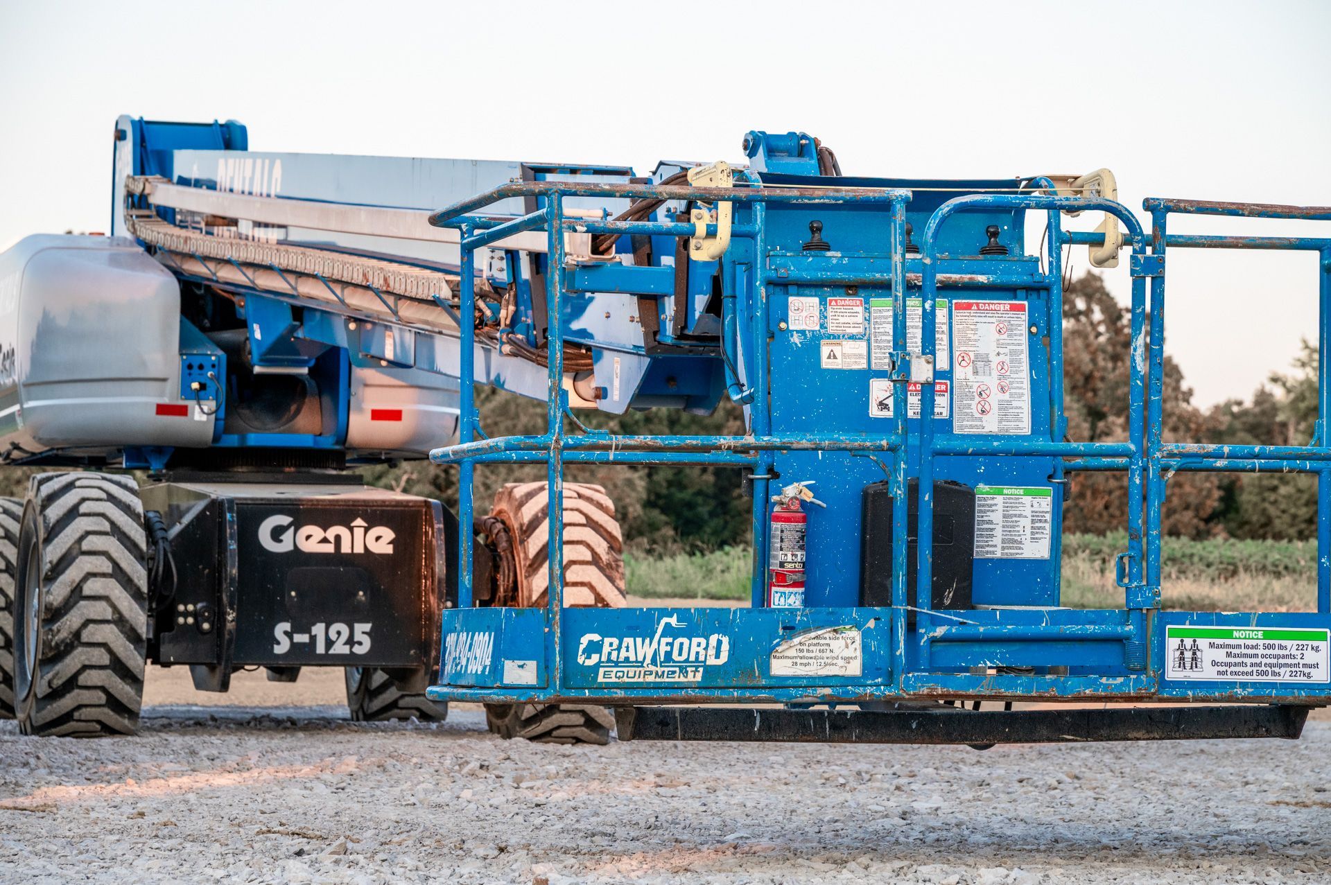 Blue Genie S-125 boom lift on gravel, outdoors.