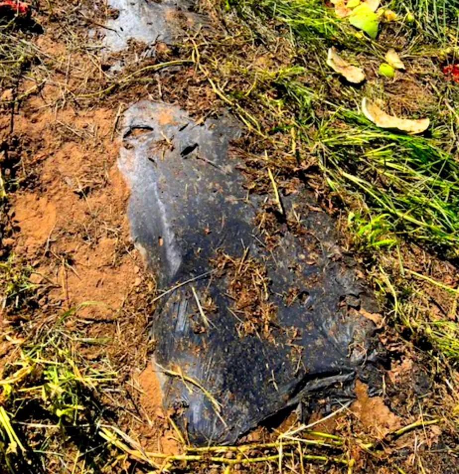 Black plastic sheet partially buried in soil and grass.
