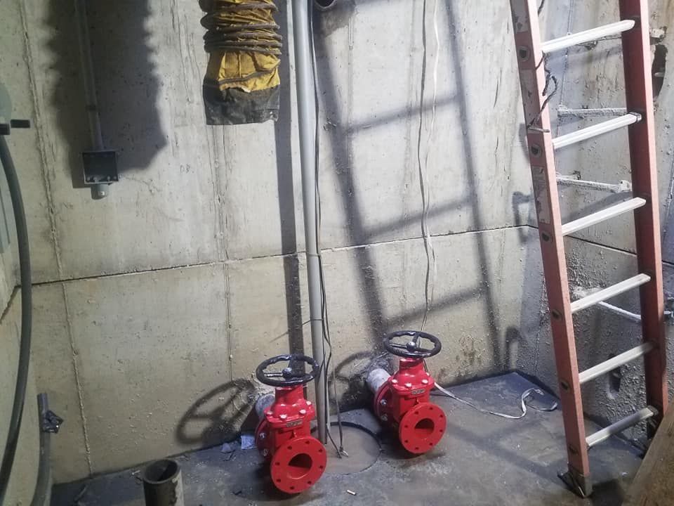 Two red valves are sitting in a room next to a ladder.