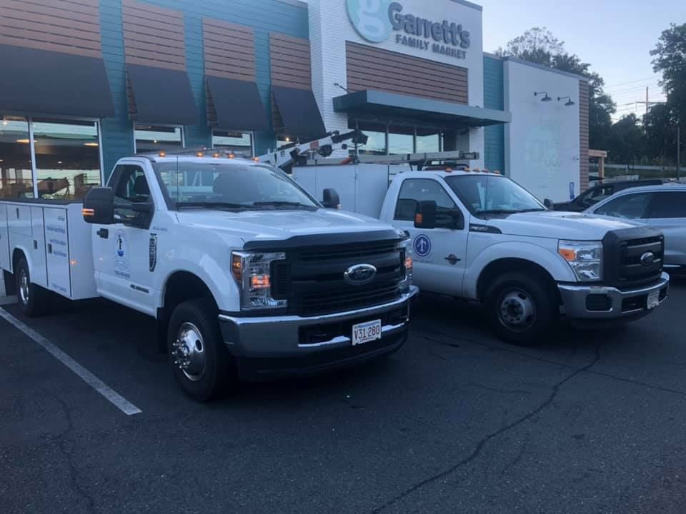 Two white trucks are parked in front of a store.