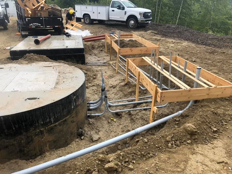 A white truck is parked in the dirt next to a large concrete cylinder.