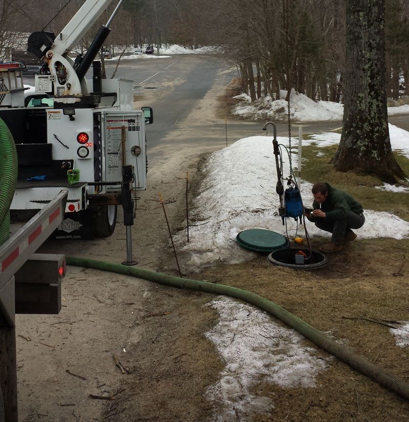 A man squatting next to a utility truck with a green hose attached to it