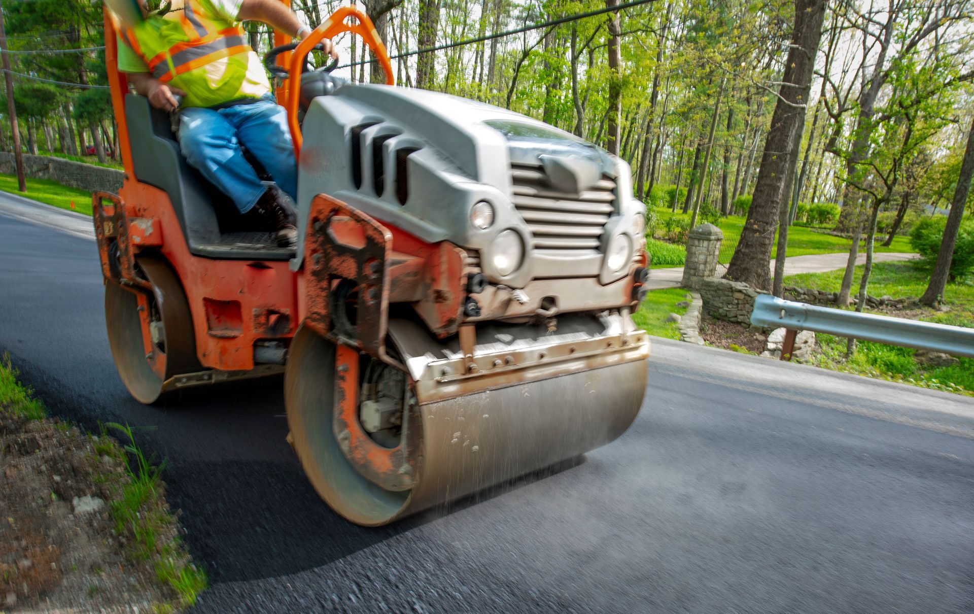 A commercial asphalt paving contractor operates a road roller to smooth asphalt on a road.