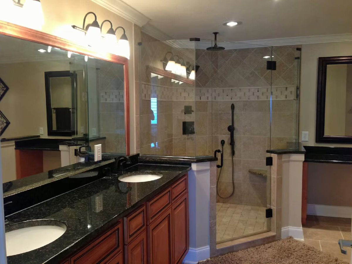 Bathroom with dual sinks, shower, and dark granite countertops.