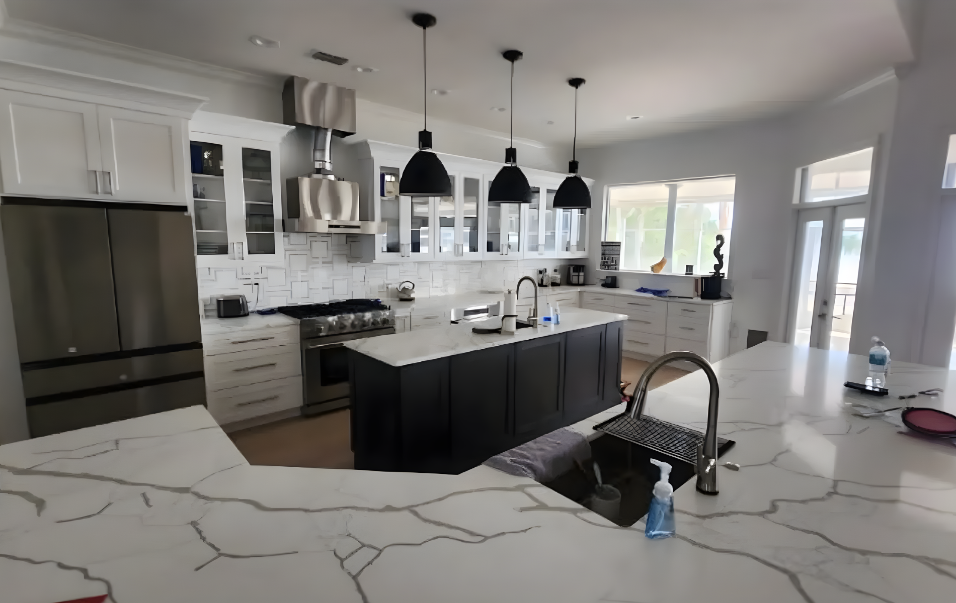 A modern, bright white kitchen with a large stainless steel refrigerator, white cabinets, and an island.