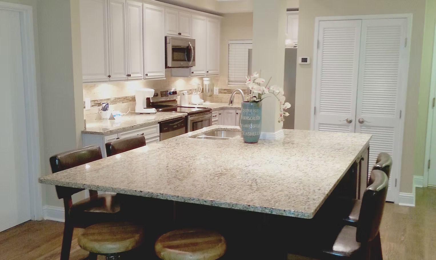 Kitchen with a granite countertop island, white cabinets, and wooden stools.