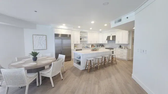 Kitchen with a dark island, stools, and cabinetry; white countertops; and a laundry room visible.