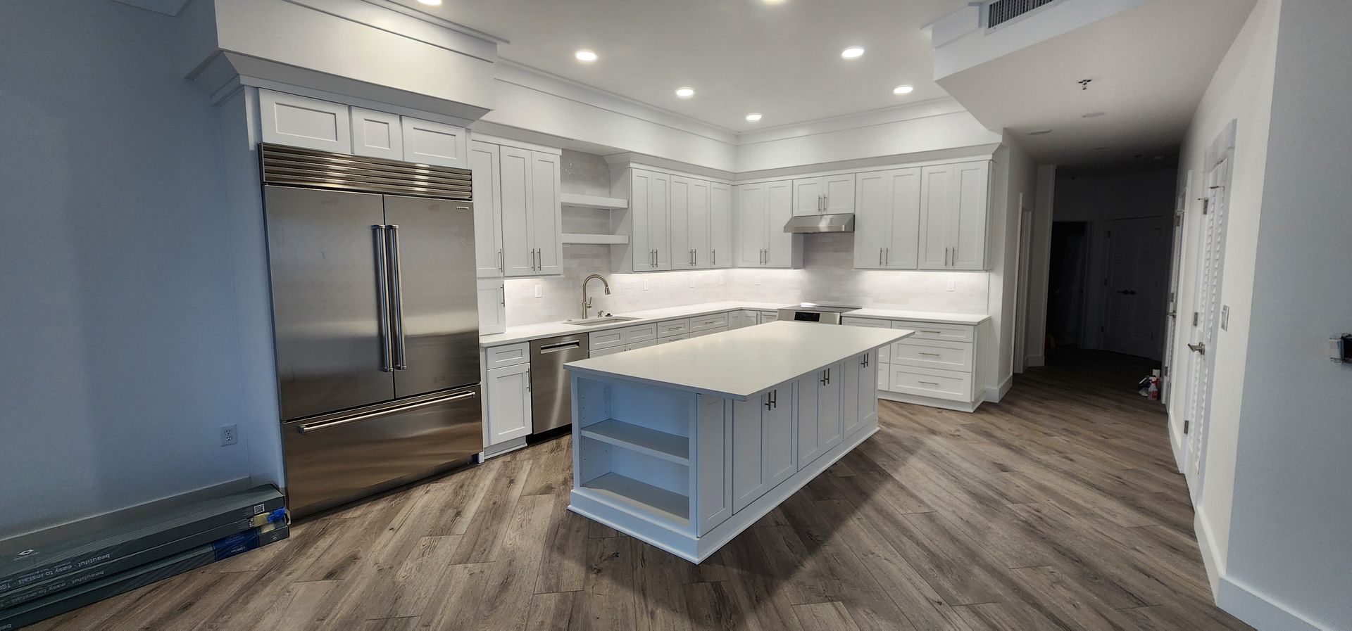 A modern, bright white kitchen with a large stainless steel refrigerator, white cabinets, and an island.