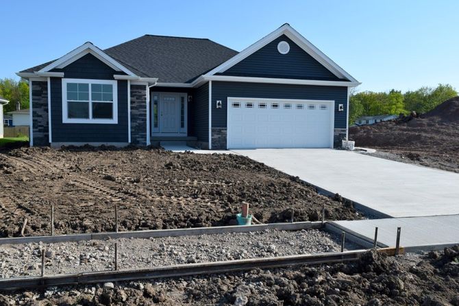 A new blue house with a white garage door sits under a clear sky. The yard is bare soil, indicating ongoing landscaping.