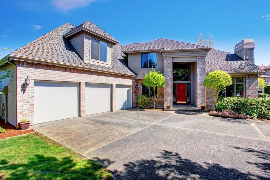 Modern two-story house with red brick facade, three-car garage, manicured trees.