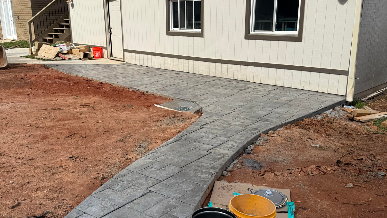 A newly constructed gray concrete path curves beside a white building with two windows.