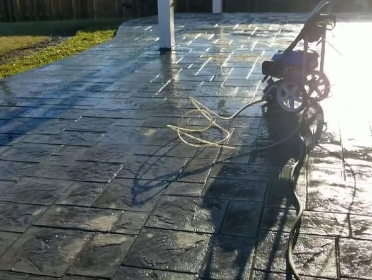 Wet tiled patio with a pressure washer casting a long shadow in the sun. The scene conveys a fresh, clean feeling.