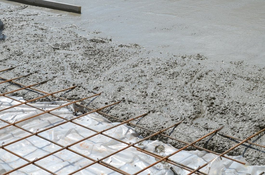 Wet concrete being poured over a grid of rusty rebar on a construction site, highlighting structure and texture.