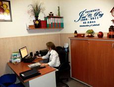 Mujer trabajando en un escritorio en una oficina; la decoración del escritorio y la pared incluye archivos y obras de arte.