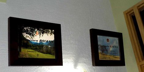 Dos cuadros enmarcados cuelgan de una pared blanca; uno muestra texto sobre un paisaje, el otro presenta un logotipo azul.