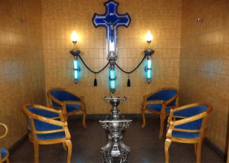 Una habitación con una cruz azul, sillas y candelabros ornamentados contra una pared de azulejos.