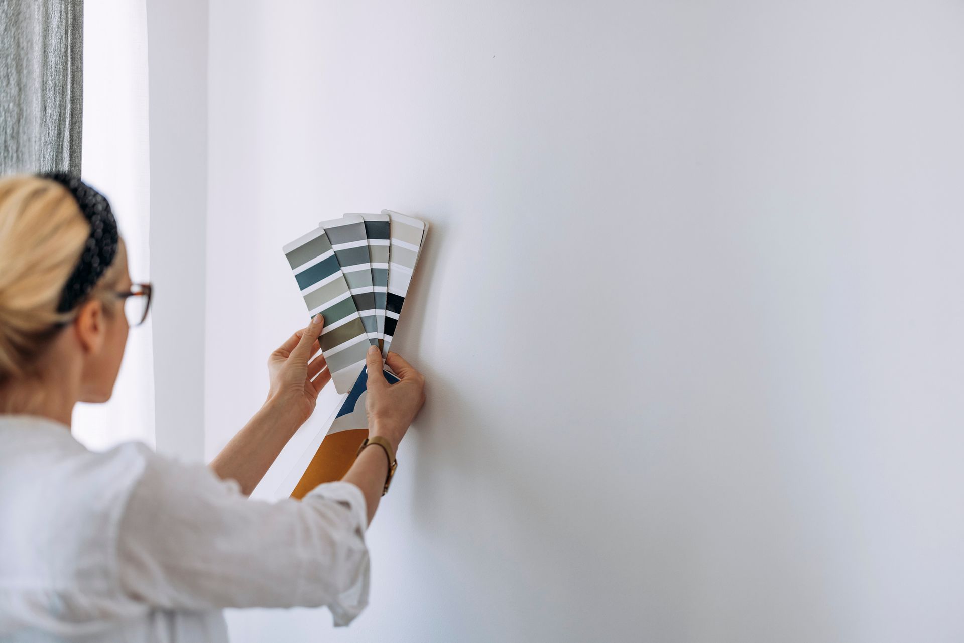 A woman is holding a palette of paint samples on a wall.