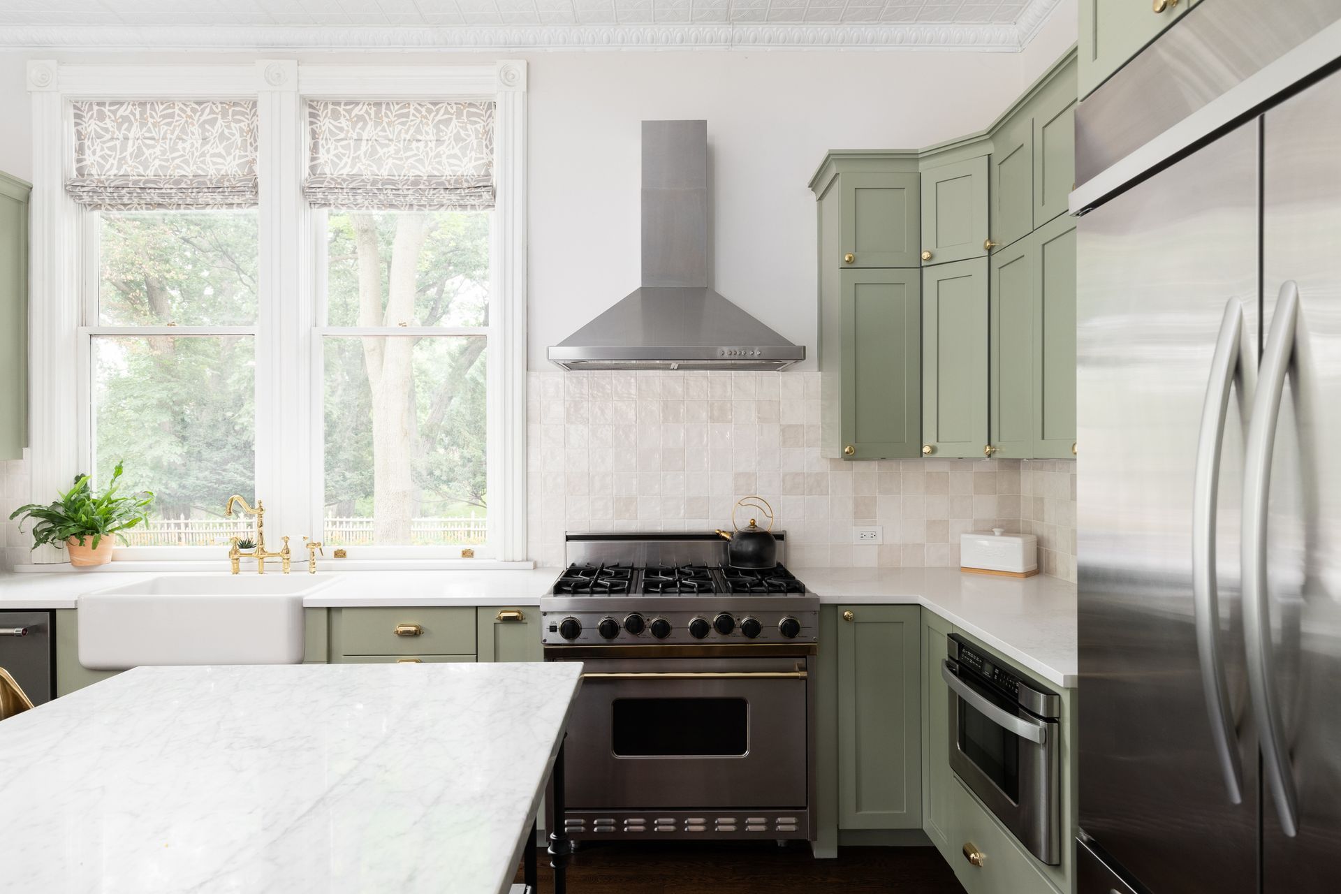 A kitchen with green cabinets , stainless steel appliances , a stove and a refrigerator.