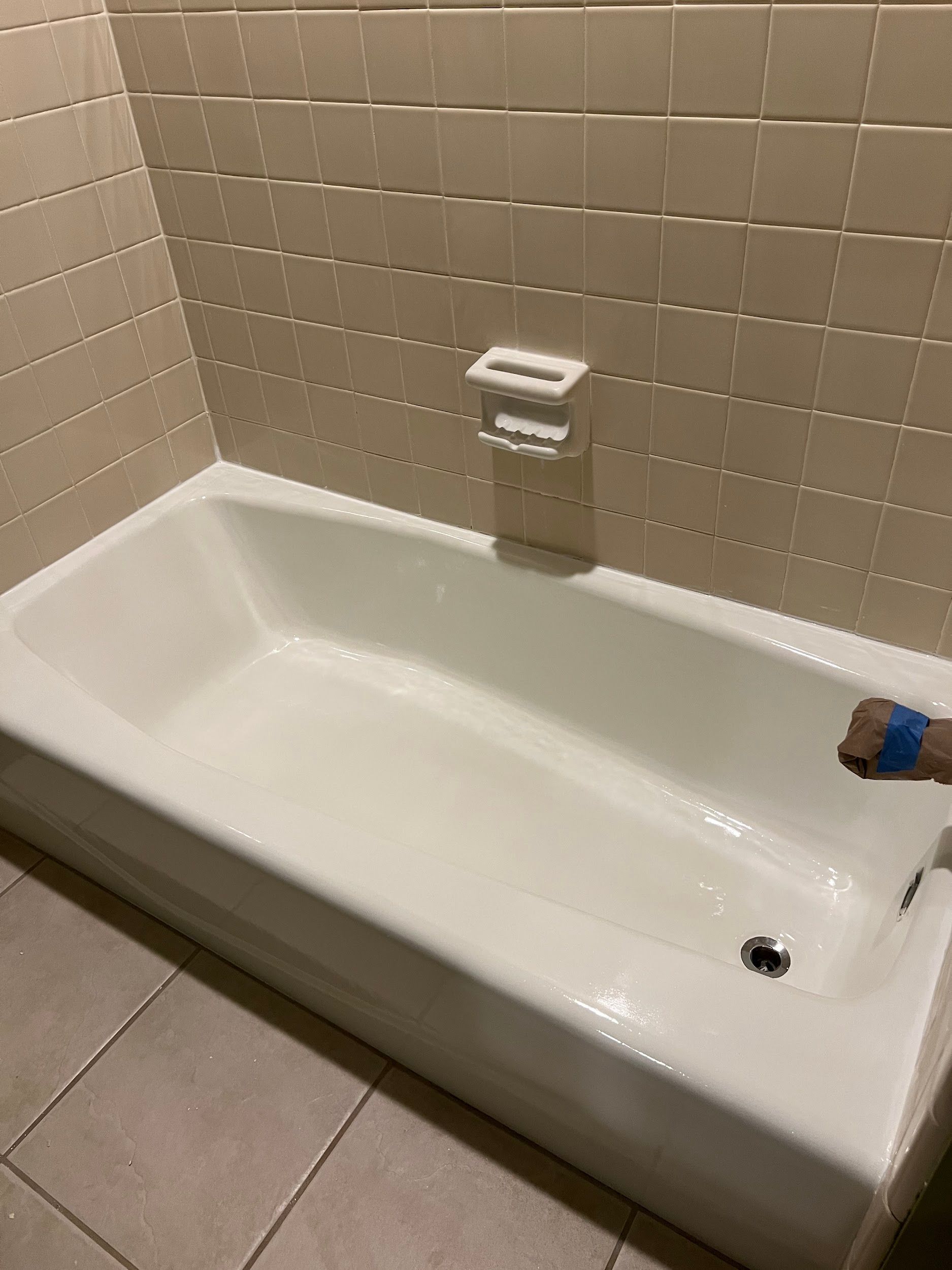 White bathtub in a beige tiled bathroom, a soap dish is mounted above the tub.