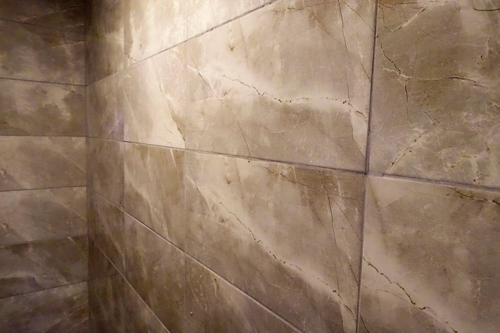 Tiled bathroom corner in shades of tan and gray, with horizontal tile pattern.