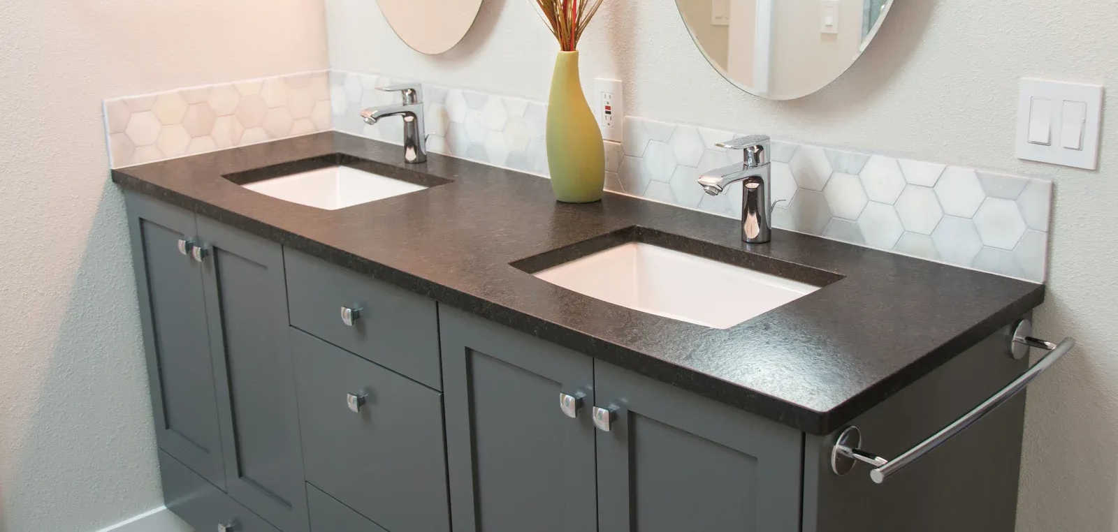 Gray double vanity with dark countertop, white sinks, and hexagonal tile backsplash.