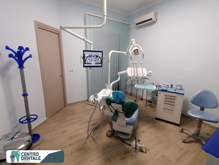 Studio dentistico con poltrona, schermo per raggi X, attrezzatura e colori blu e bianco.