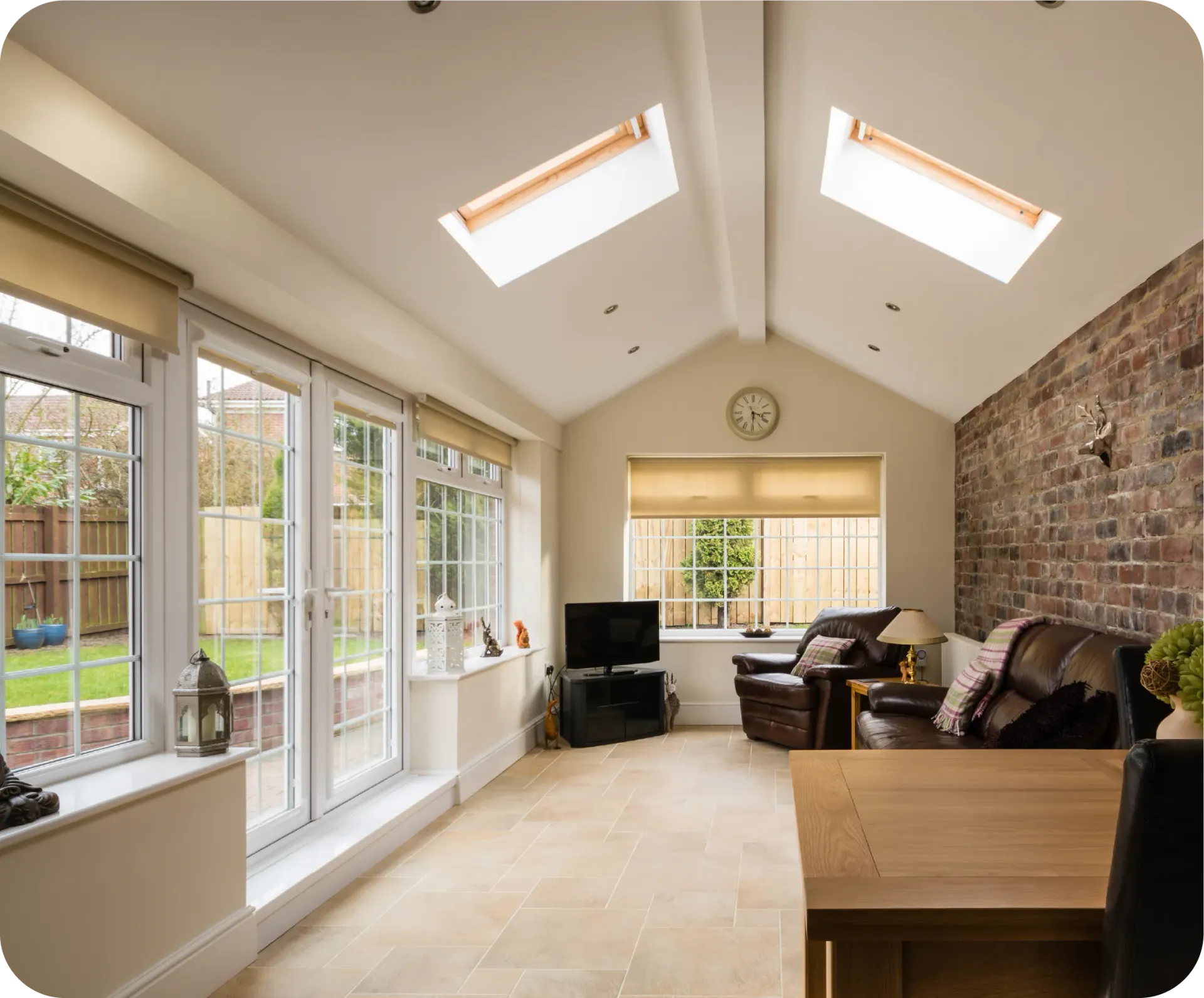 Sunroom with skylights, large windows, brick accent wall, furniture, and a view of a backyard.