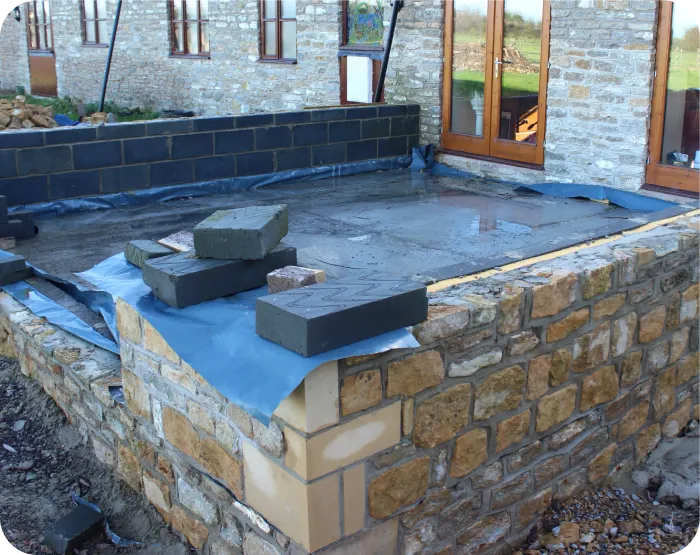 Construction of a stone patio with a concrete base and retaining walls.