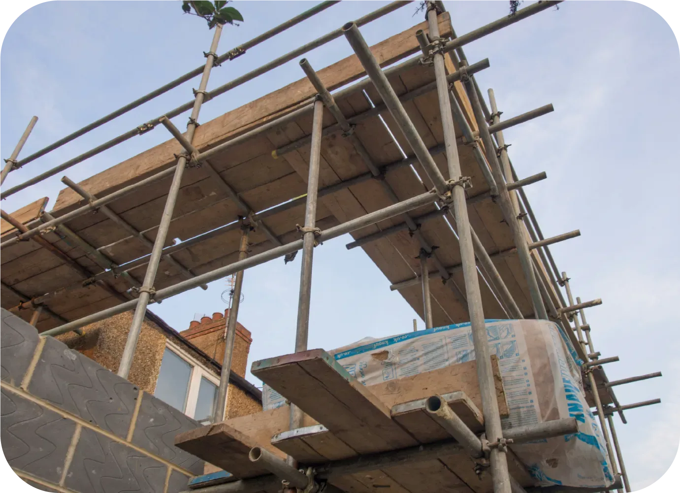 Scaffolding on a brick building under construction; grey and wooden structure with a cloudy sky.