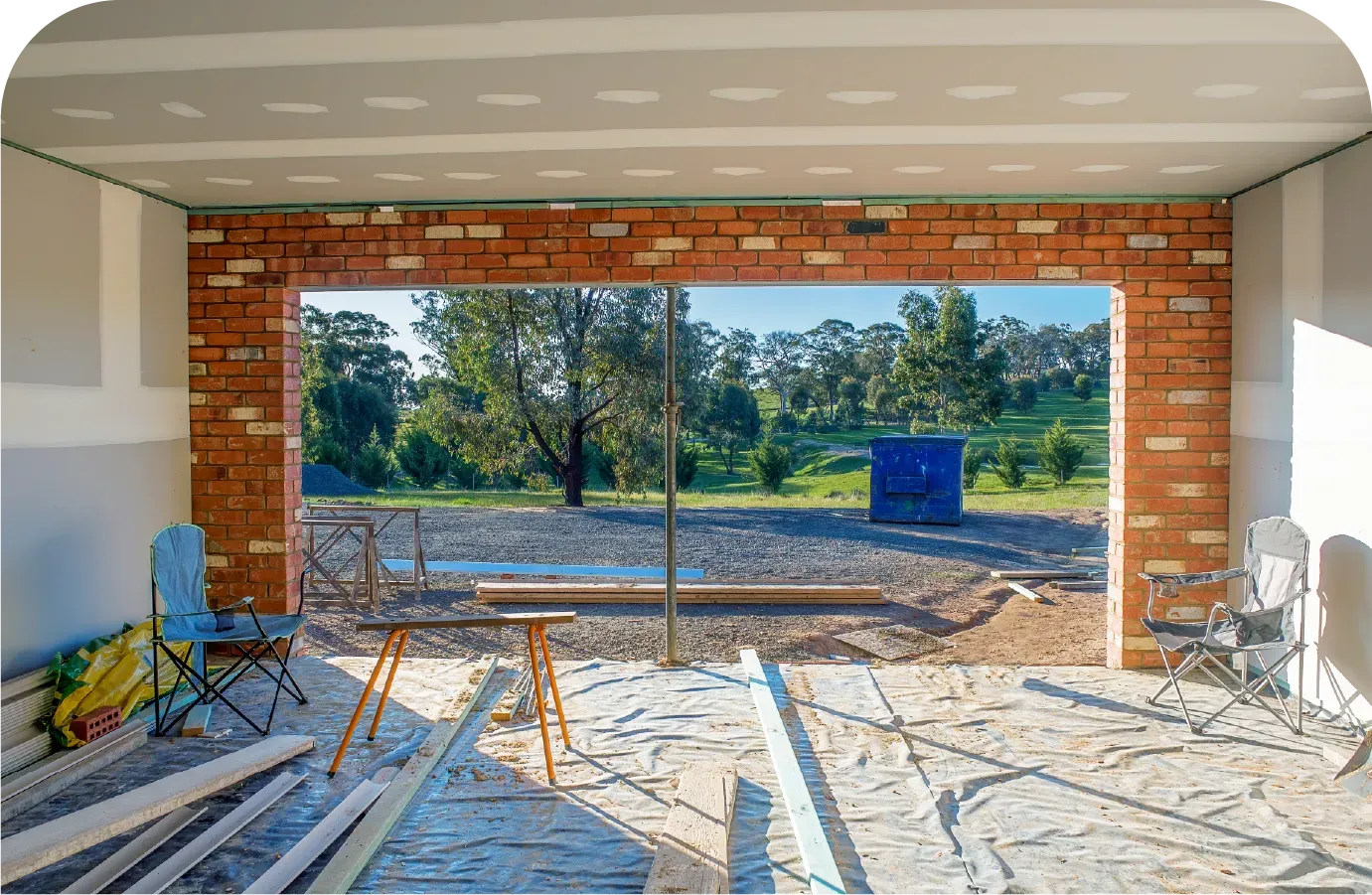 Interior of a room under construction, open to a sunny outdoor view. Brick border frames the opening.