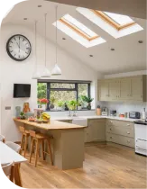 Kitchen with skylights, island with stools, light-colored cabinets, and large clock.