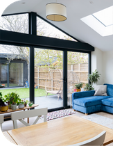 Living room with large glass doors overlooking a backyard, blue sofa, plants, and a light-colored wooden table.