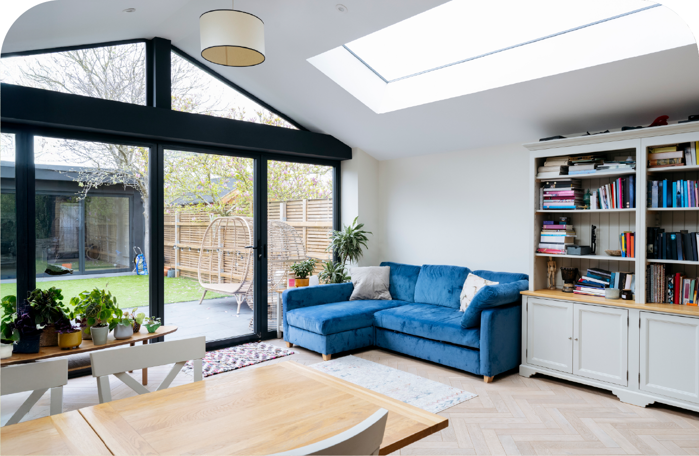 Bright living room with blue sectional, glass doors to garden, skylight, and white bookshelf.