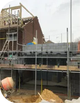 Construction site: brick house under construction, scaffolding, lumber, cement mixer, sand pile.