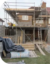 House under construction with scaffolding; exposed brick, cinder blocks, wood, and insulation.