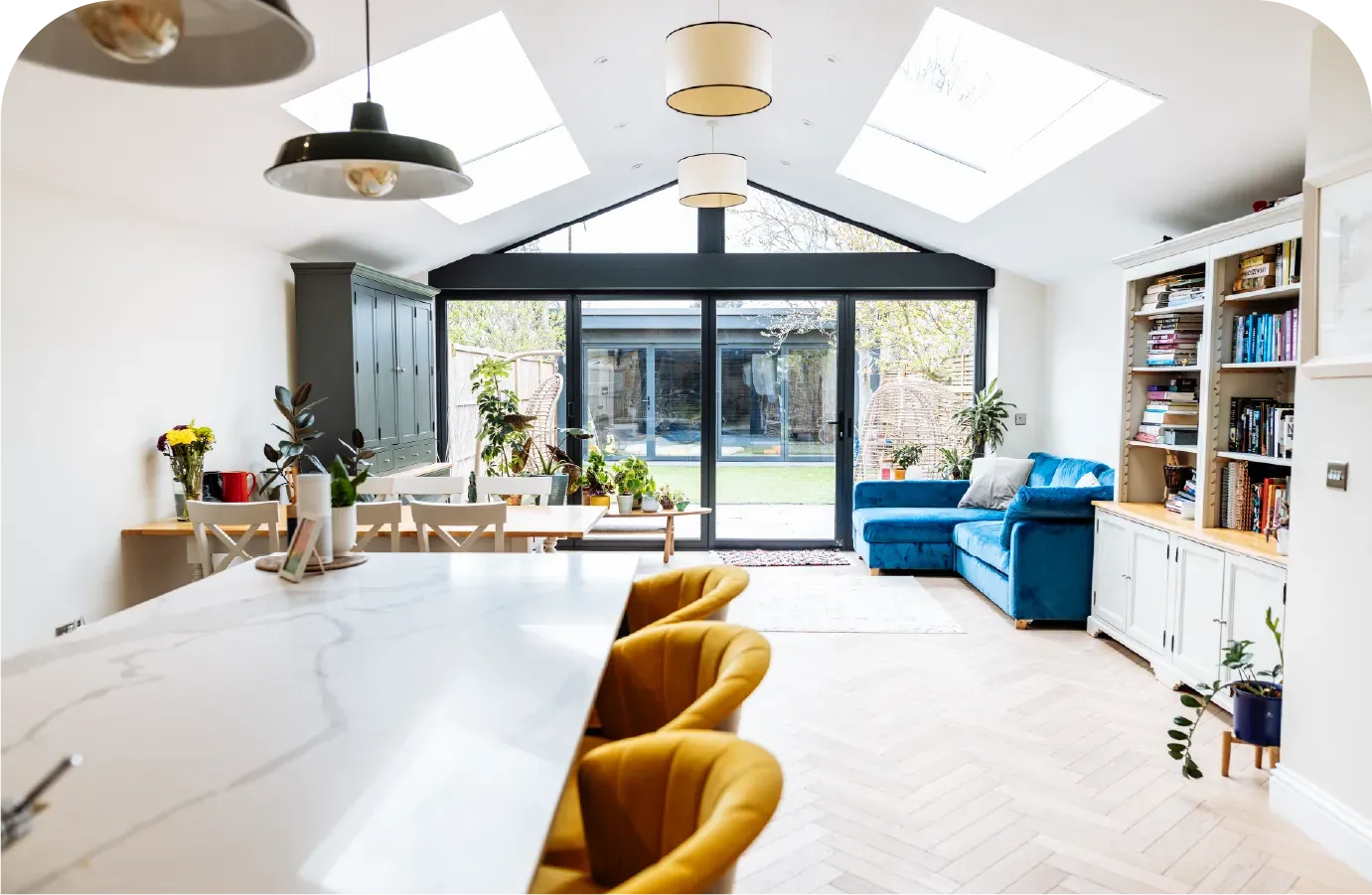 Spacious kitchen with island, seating, and open to a living area with blue sofa, white walls, and glass doors to a backyard.