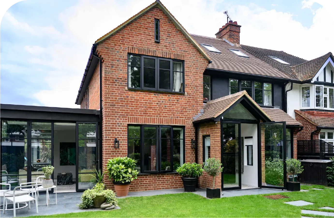 Brick home with black-framed windows and a glass-enclosed entrance and side extension, set on a green lawn.