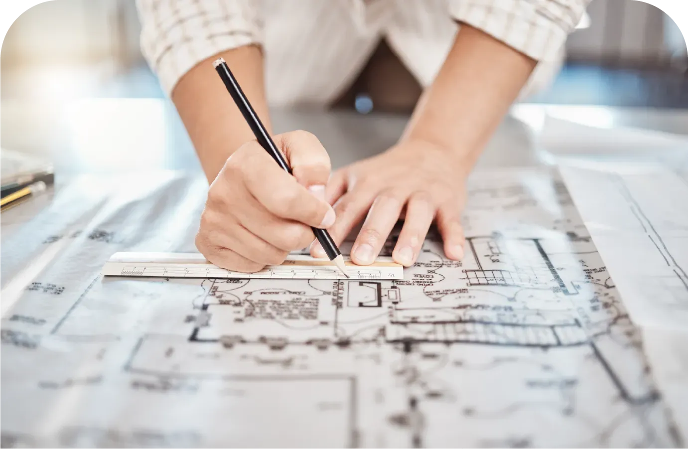 Hands using a ruler and pencil to draw on architectural blueprints.