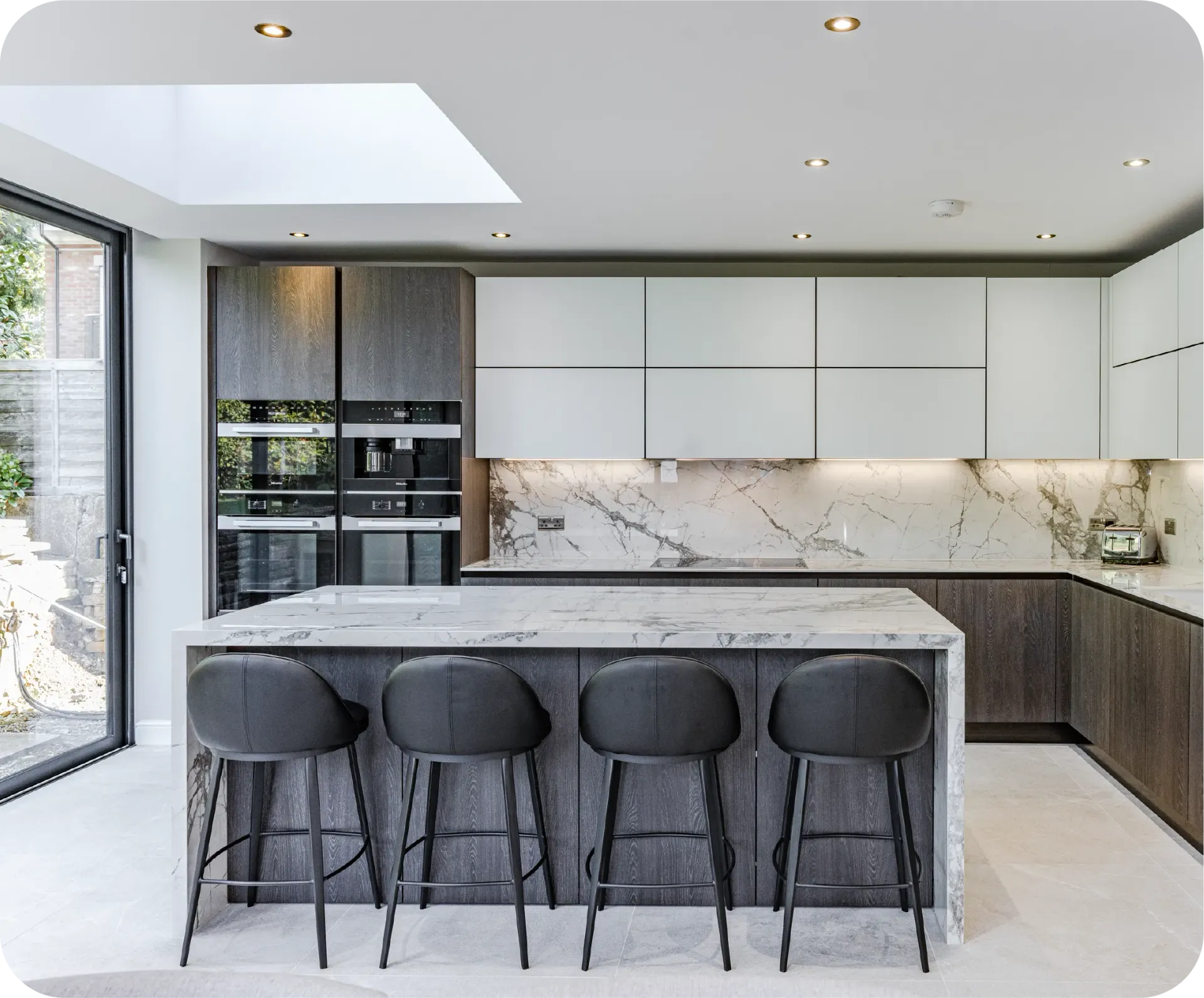 Modern kitchen with island, gray and white cabinets, marble countertops, and four bar stools.