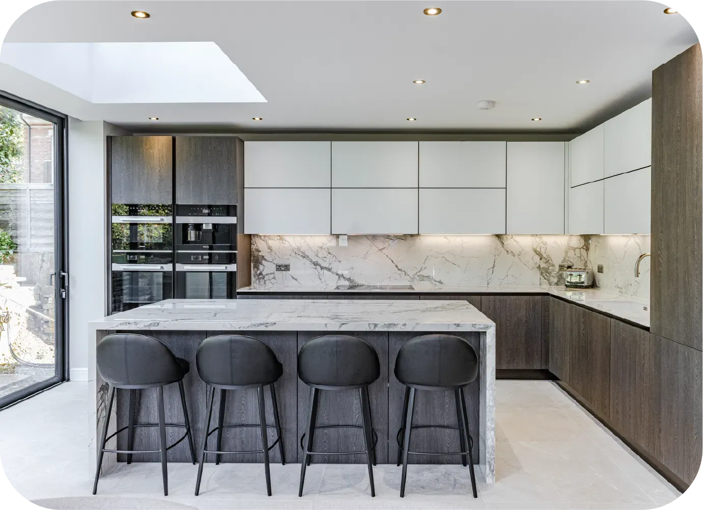 Modern kitchen with island, gray cabinetry, marble countertops, and four bar stools.