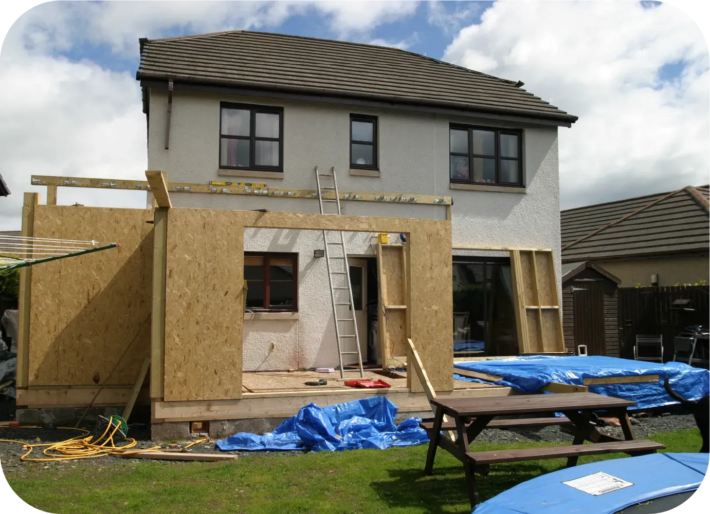 House under construction with extension framed in wood; back yard setting.