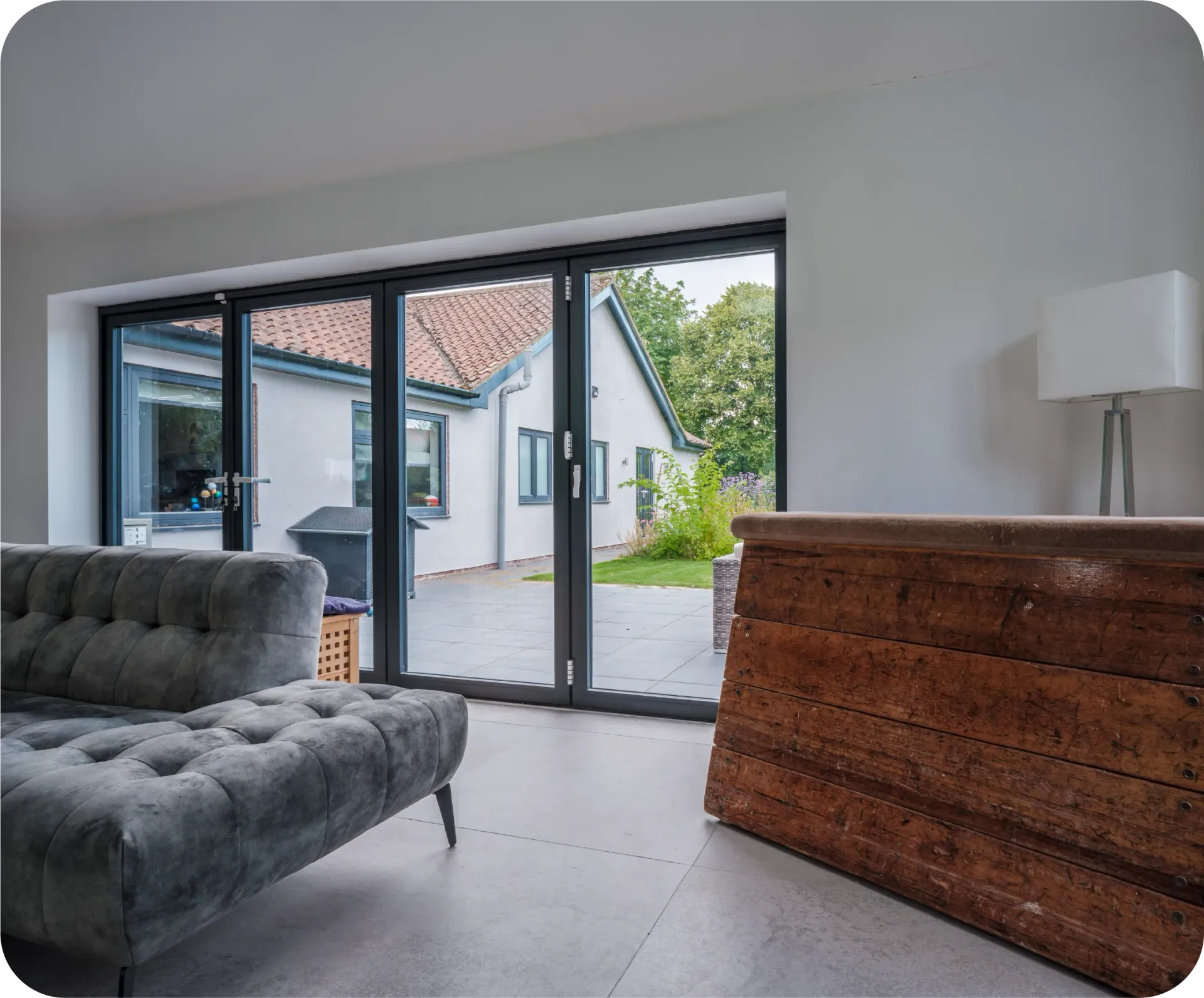 Living room with gray sofa, wooden chest, and glass doors leading to a patio and house.