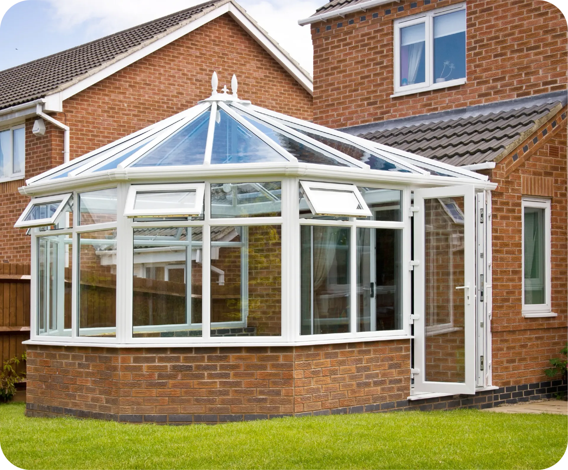 Sunroom addition to a brick house with a glass roof and white frames.
