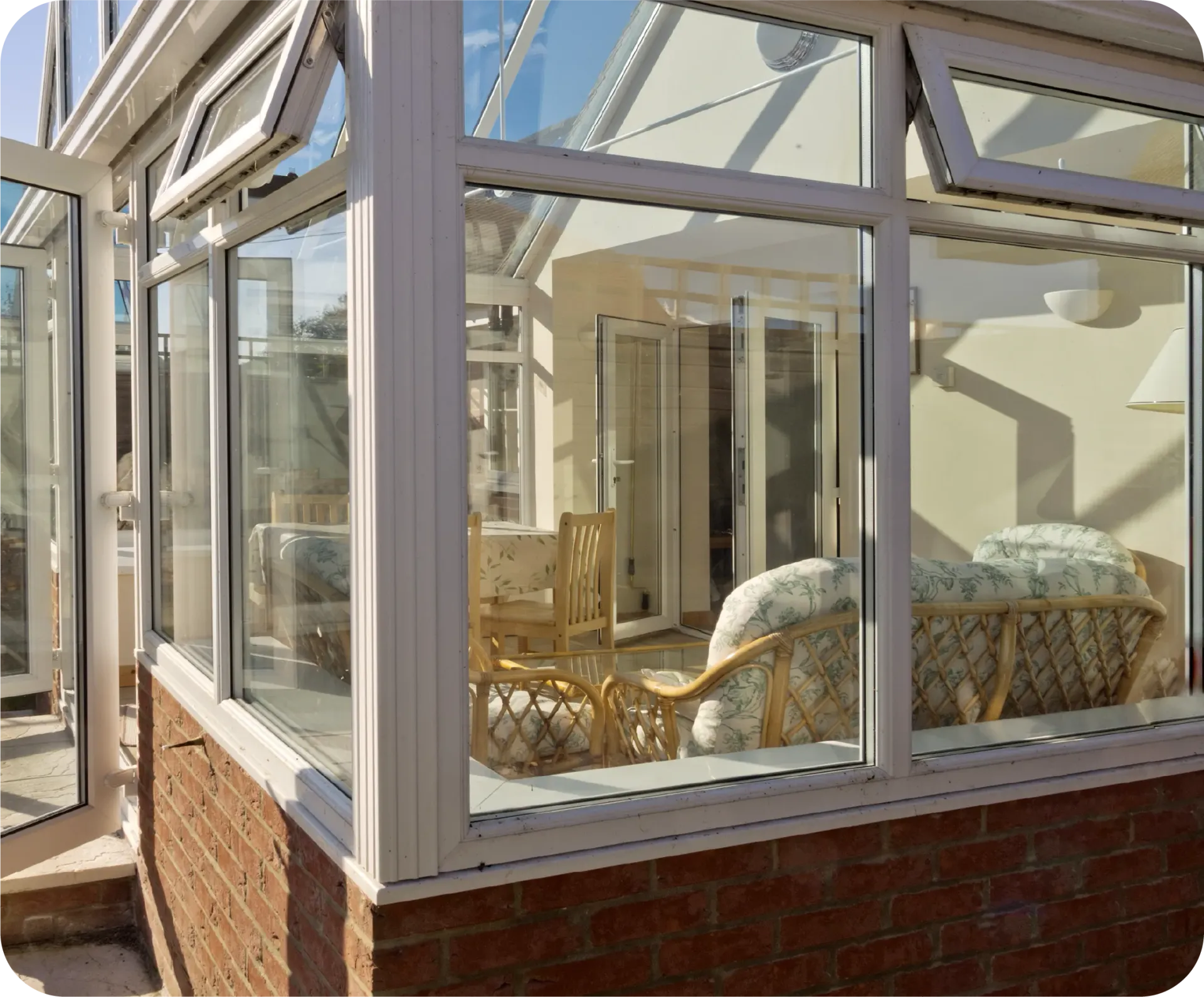 Sunroom with white frames, glass windows and brick base, filled with furniture, doors open.