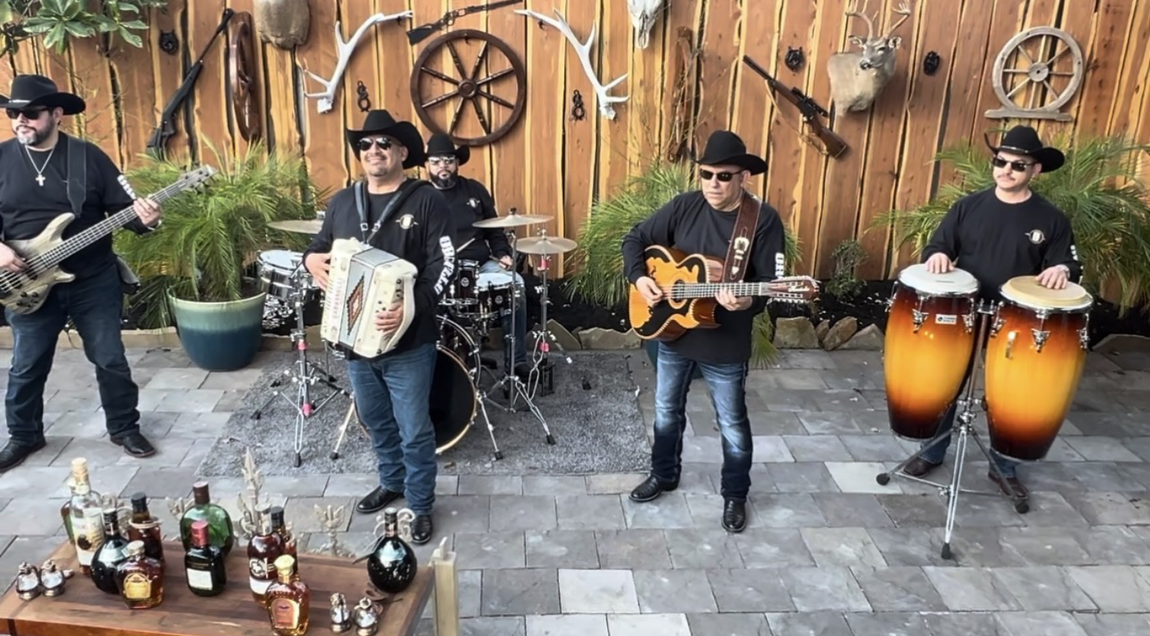 Grupo Orgullo playing instruments in front of a wooden fence.