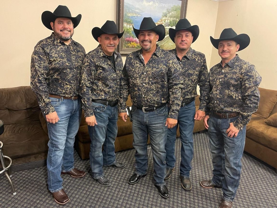 Grupo Orgullo wearing cowboy hats are standing next to each other in a living room.