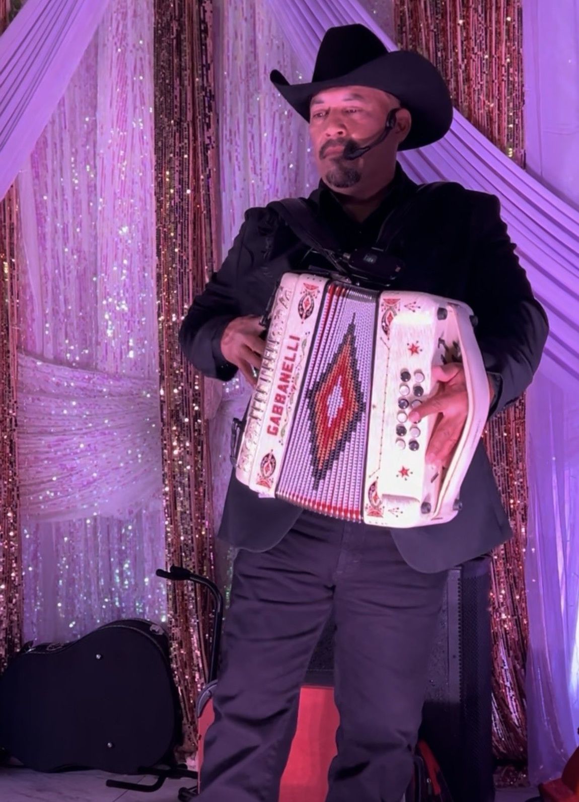 A member of grupo orgullo in a cowboy hat is playing an accordion on stage.