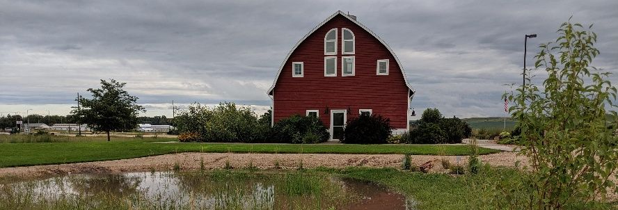 The Sandhills Journey visitor center stands behind a small pond under a cloudy, overcast sky.